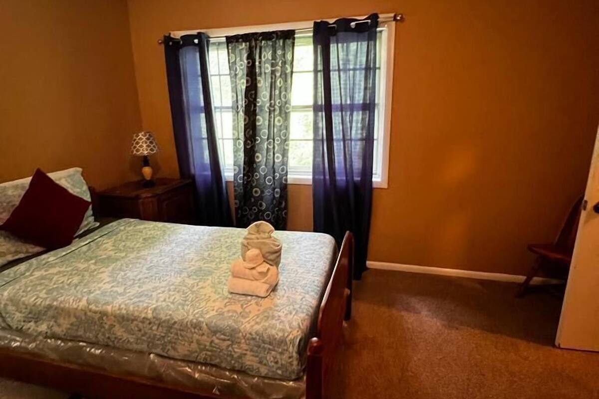 A bedroom with a bed, a nightstand, a lamp, and a window with curtains.