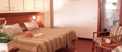A hotel room with a bed, two chairs, a small table, an air conditioning unit, and a bathroom visible through an open door.