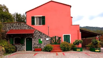A red two-story house with a stone facade, green shutters, and a small porch.