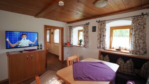 Una habitación acogedora con techo de madera, un televisor en un mueble bajo, una cama con manta morada, una mesa de madera y un sofá con cojines escoceses.