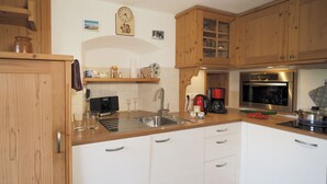 Una cocina con armarios de madera, un lavamanos de acero inoxidable, una cafetera y un microondas.