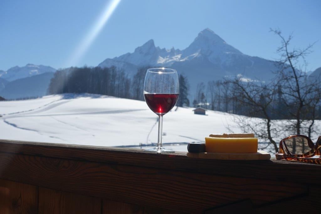 Una copa de vino tinto sobre una mesa de madera, con vistas a la montaña al fondo.