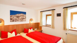 Una cama doble con ropa de cama roja y blanca, una mesita de noche con un vaso y una lámpara de pared.