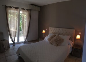 Relax in this serene room with a large bed, tufted headboard, and two bedside lamps, surrounded by a view of lush greenery.