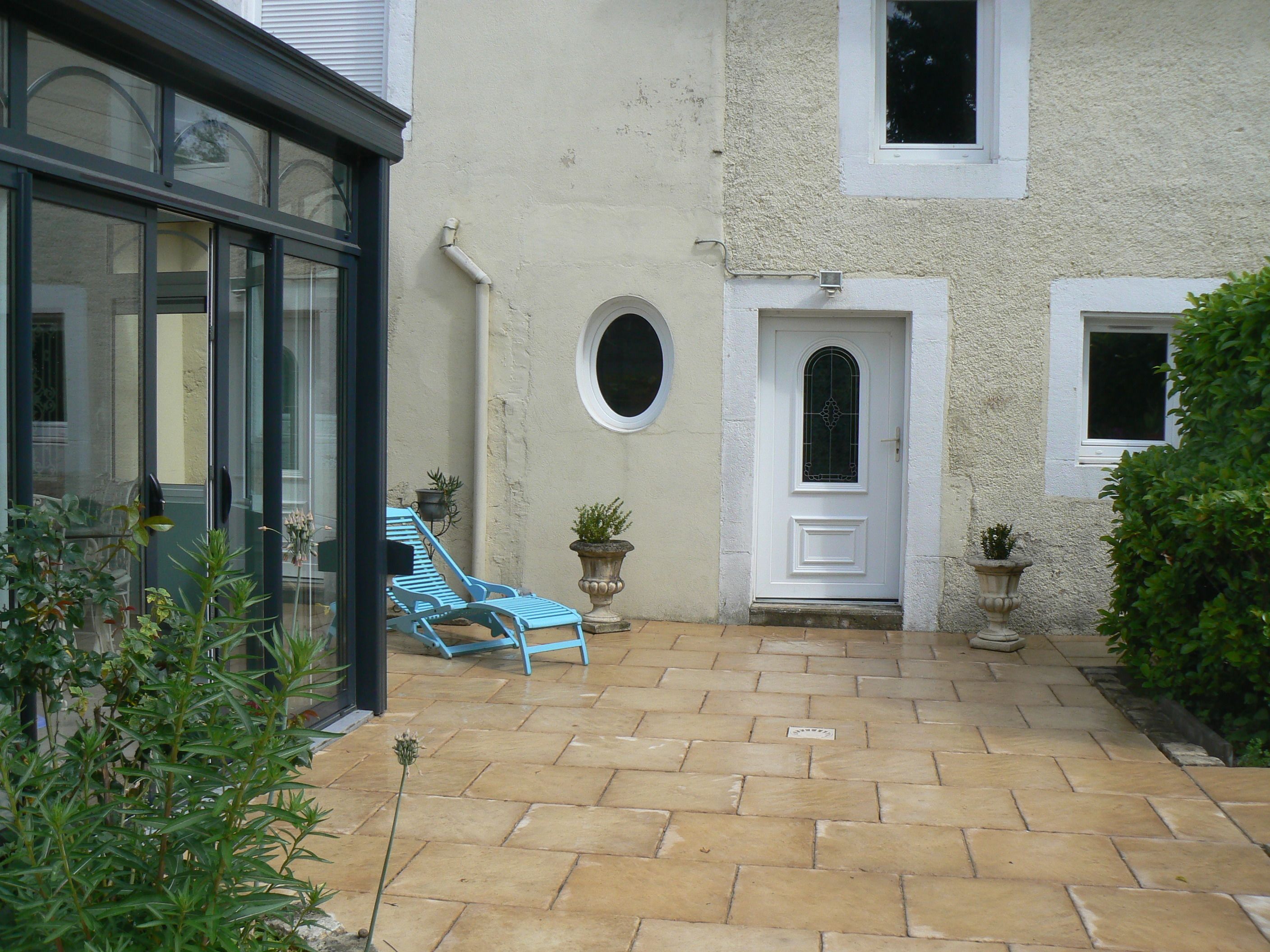 Ein Innenhof mit einer gefliesten Terrasse, einer weißen Tür und einem blauen Stuhl.