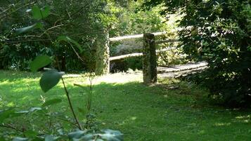 A rustic wooden gate in a lush green garden with dense foliage and a stone wall in the background.