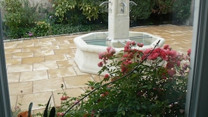 A courtyard with a fountain, stone tiles, and lush greenery. - La Maison de l'étang (Sampigny)