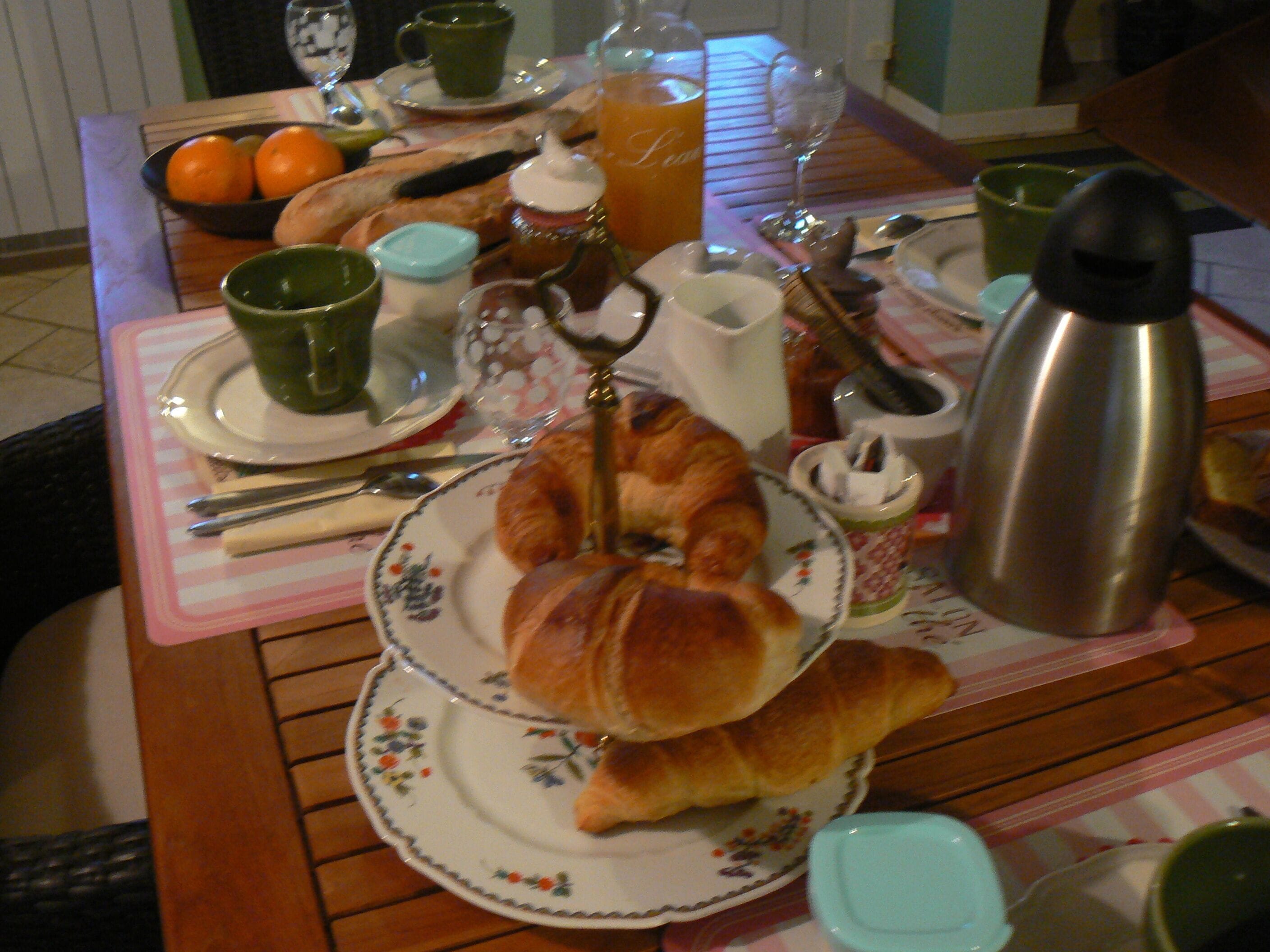 A breakfast table with croissants, a thermos, and a fruit bowl.