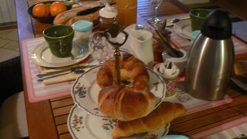 A breakfast table with croissants, a thermos, and a fruit bowl.