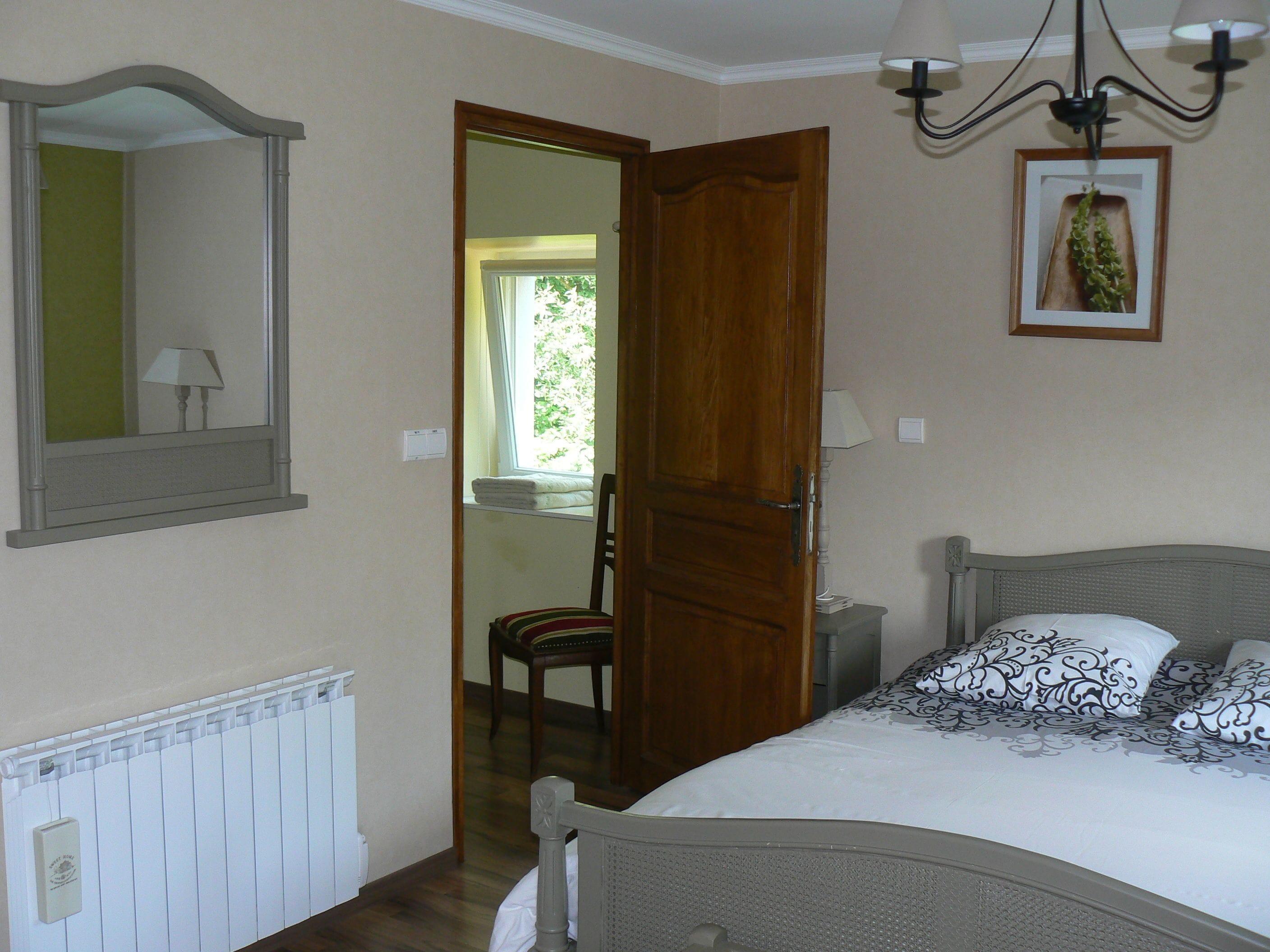 Ein Schlafzimmer mit einem Bett, einem Sessel, einem Heizkörper, einem Spiegel und einer Tür zu einem anderen Raum.