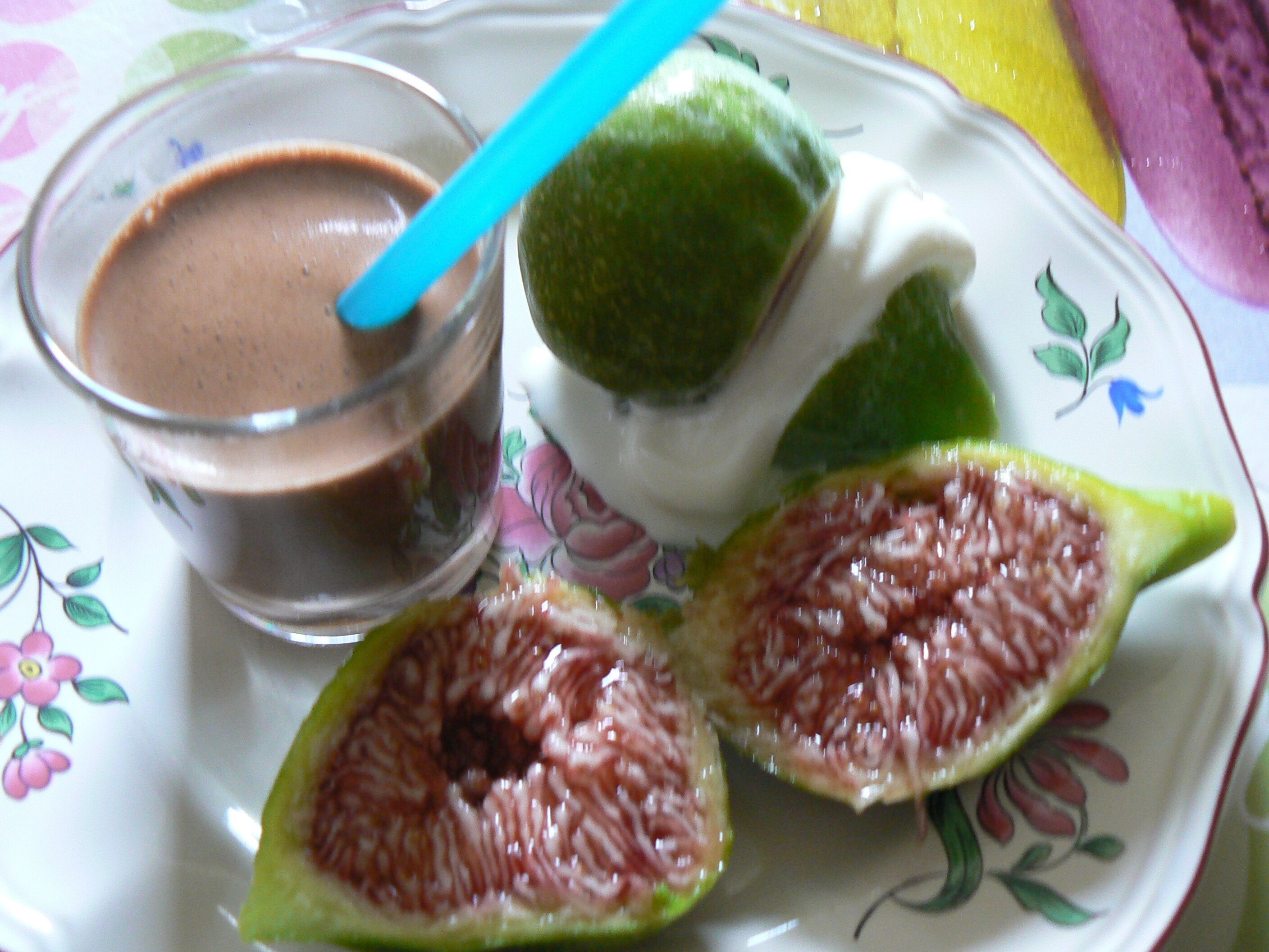 A plate with a glass of chocolate drink, a lime half, and a slice of green fruit.