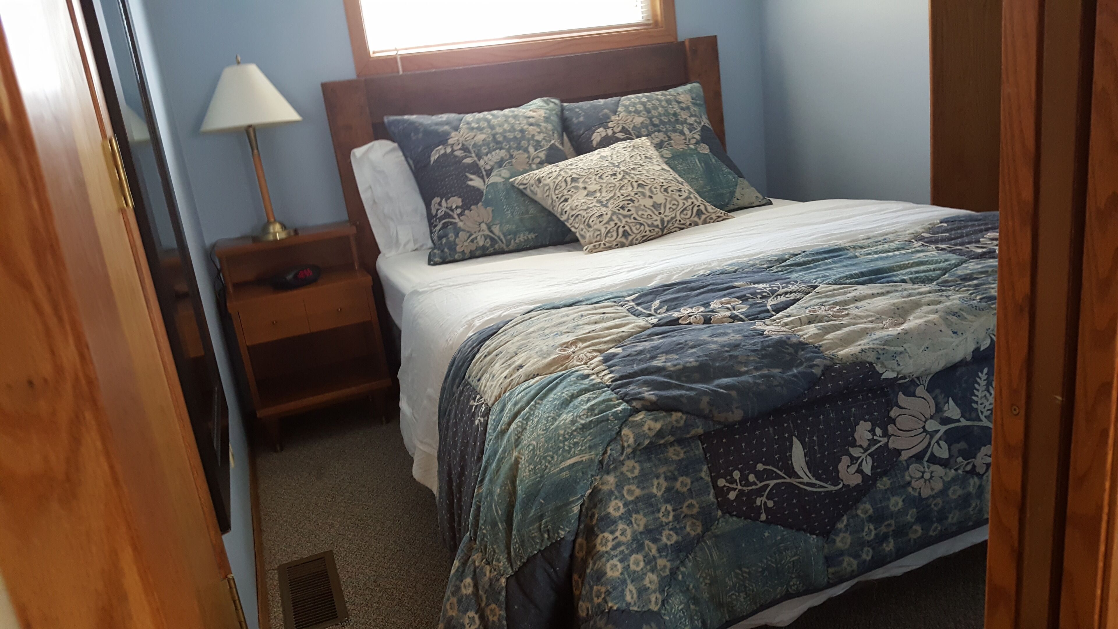 A bedroom with a bed, a nightstand, a lamp, and a window.