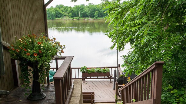 A wooden deck with a bench and railing overlooking a calm lake, surrounded by lush greenery.
