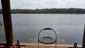 A view from a window overlooking a lake with a chair in the foreground.