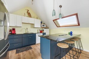 Una cocina con una isla central, taburetes de bar, microondas y refrigerador.