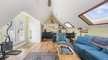Un loft espacioso con techos altos, una zona de cocina, un sofá azul y un tragaluz.