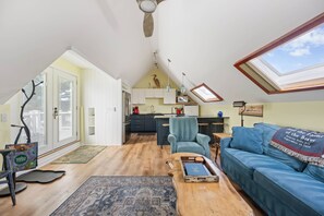 Un loft espacioso con techos altos, una zona de cocina, un sofá azul y un tragaluz.