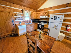 A wooden cabin kitchen with a wooden table, chairs, a sink, stove, and refrigerator. - Kelci Kabin a Cozy Cabin with Mtn View, Hot Tub and very private. (Sevierville)