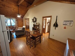 A cozy, wooden-floored living area with a dining table, chairs, a sofa, and a refrigerator.