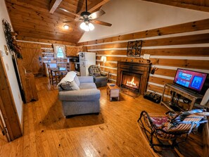 A cozy living room with a fireplace, a television, and a dining area. - Kelci Kabin a Cozy Cabin with Mtn View, Hot Tub and very private. (Sevierville)
