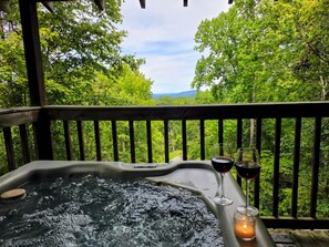 A hot tub with a glass of red wine and a candle on a wooden deck with a forest view. - Kelci Kabin a Cozy Cabin with Mtn View, Hot Tub and very private. (Sevierville)