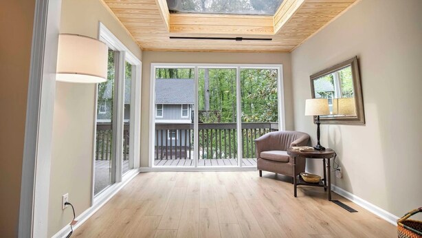 A room with a skylight, large sliding glass doors, a wooden floor, a chair, a lamp, and a framed picture on the wall.