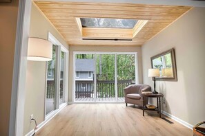 A room with a skylight, large sliding glass doors, a wooden floor, a chair, a lamp, and a framed picture on the wall. - The Tiger's Den - Walk to downtown Clemson! (Clemson)