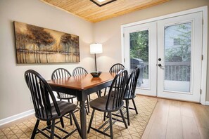 A dining area with a wooden table and black chairs, a painting on the wall, a floor lamp, and a sliding glass door with blinds.
