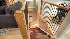 A wooden staircase with a handrail, a dining area with chairs, and a sofa in the background.