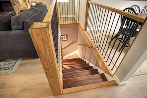 A wooden staircase with a handrail, a dining area with chairs, and a sofa in the background.