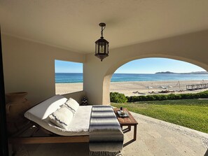 A bedroom with a view of the beach, a bed, a nightstand, and a hanging light fixture.