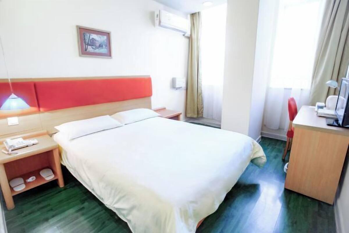 A hotel room with a bed, a desk, a chair, a nightstand, a lamp, and a window with curtains.