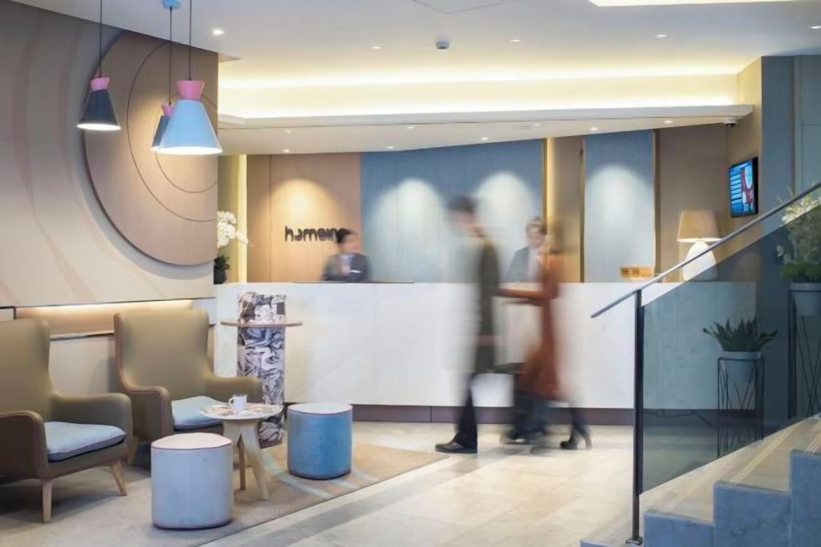 A hotel reception area with a reception desk, seating area, and a staircase.