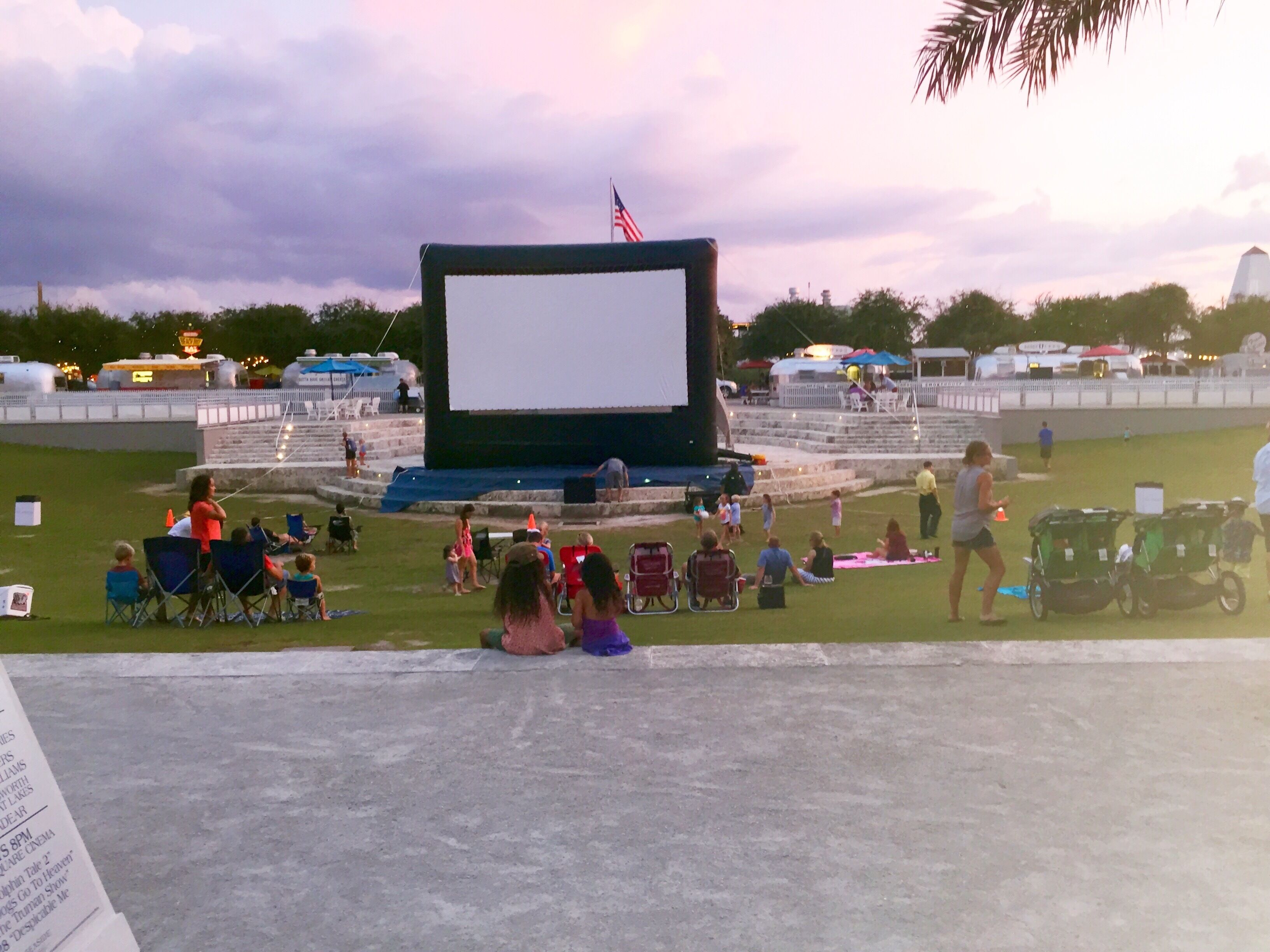 An outdoor movie theater with a large screen, seating, and a stage.