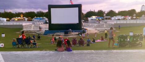 An outdoor movie theater with a large screen, seating, and a stage.