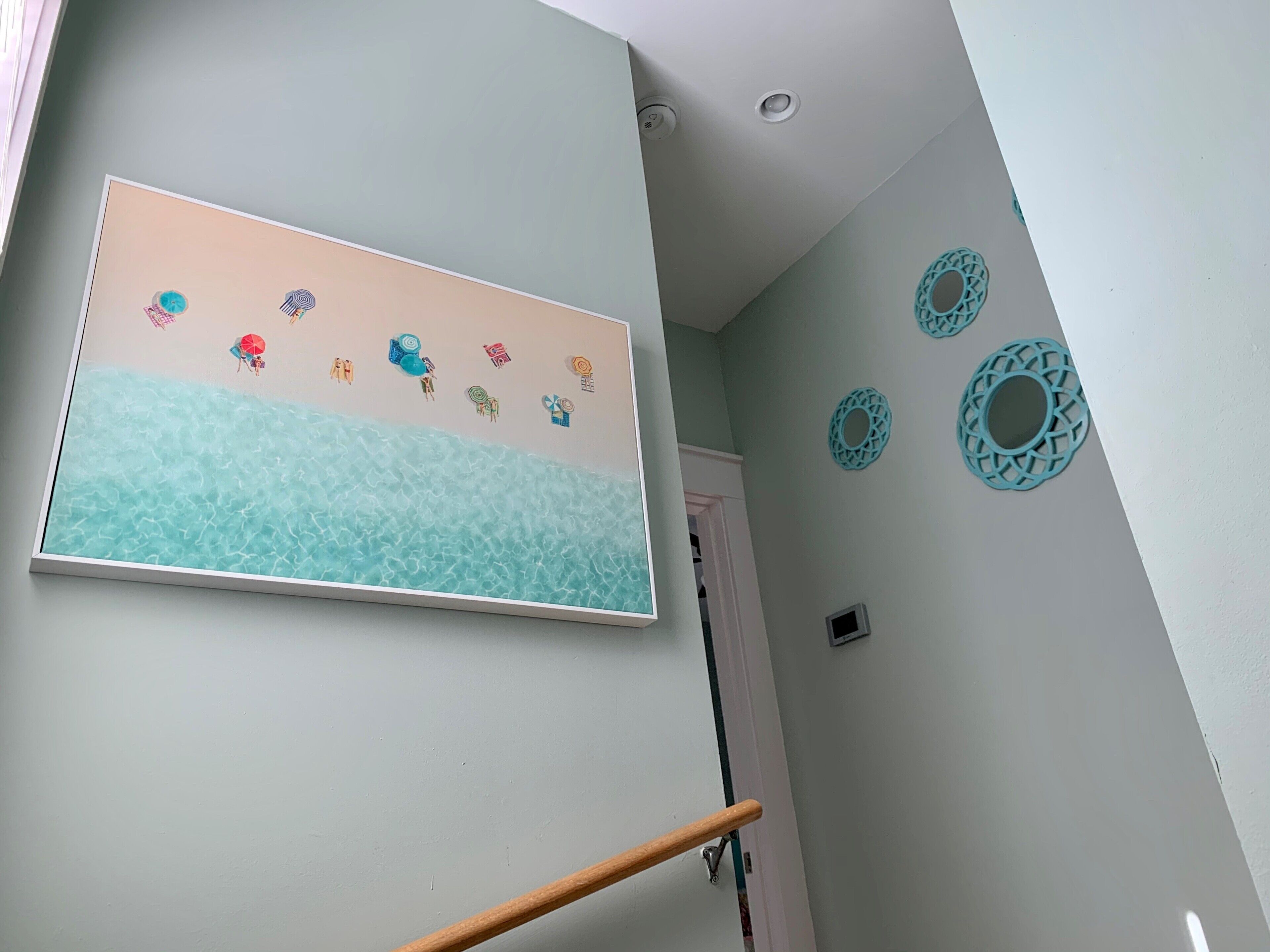 A hallway with a wall-mounted artwork depicting a beach scene, a door, and decorative wall plates.