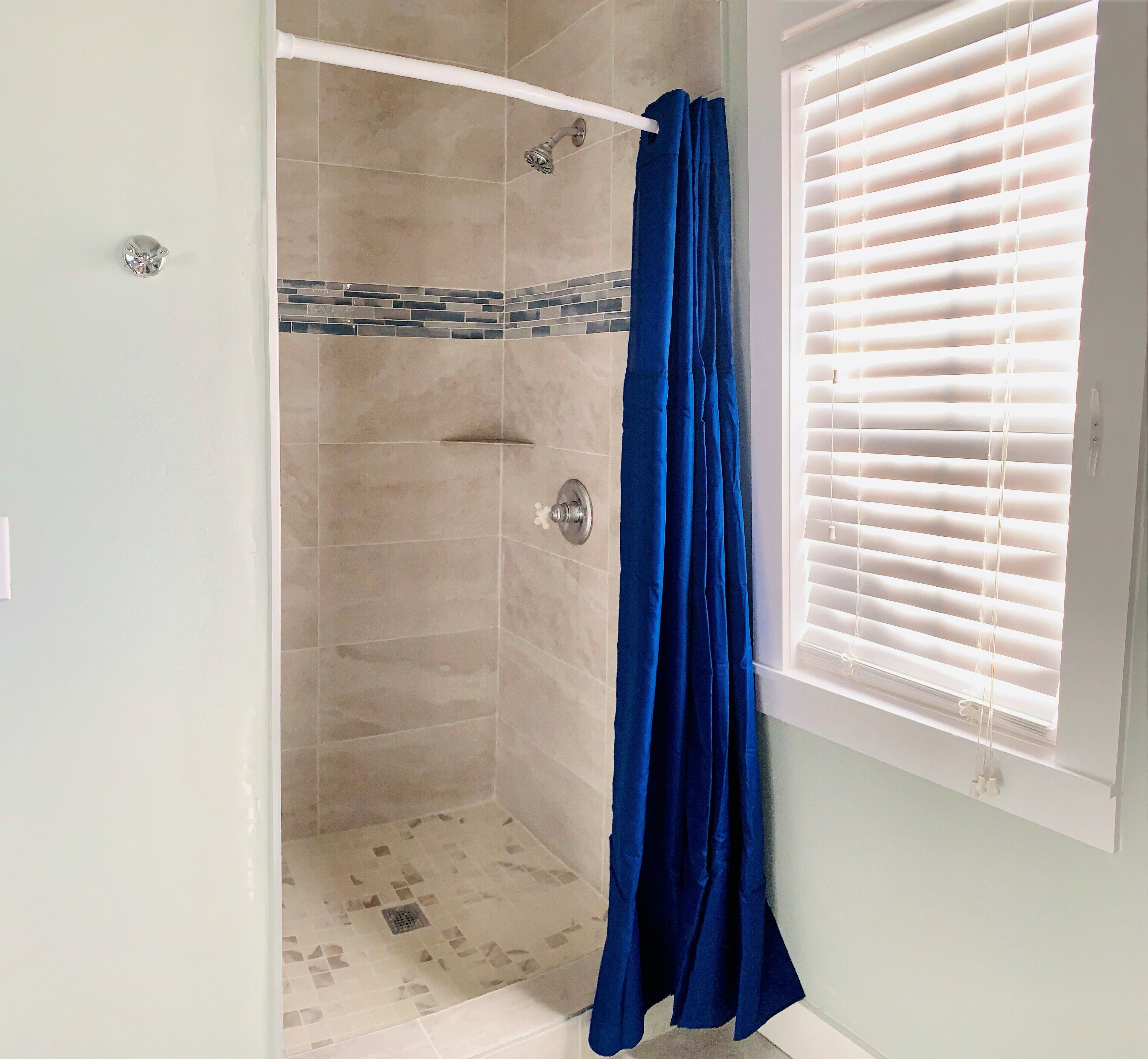A shower with beige tiles and a blue shower curtain.
