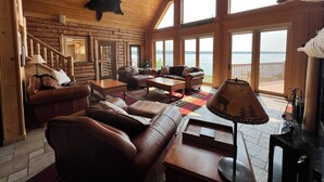 L’intérieur d’une cabane en rondins, avec une grande fenêtre donnant sur un plan d’eau, est aménagé avec des canapés en cuir et une table basse.