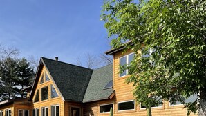 Un bâtiment en bois à deux étages, doté d’une terrasse, d’un espace extérieur aménagé pour s’asseoir et d’une grande fenêtre.