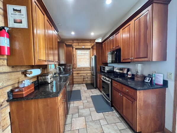 A kitchen with wooden cabinets, a stainless steel refrigerator, a microwave, a stove, and a sink. - Log Cabin w/indoor pool on Lake, 30 Min from Wis Dells! 8 min. from Sand Valley (Arkdale)