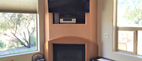 A living room with a fireplace, a television mounted above it, and a bookshelf with books.