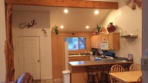 A compact kitchen with wooden cabinets, a central island with bar stools, a white trash bin, and a window with a view. - Moab Rim Village Oasis (Moab)
