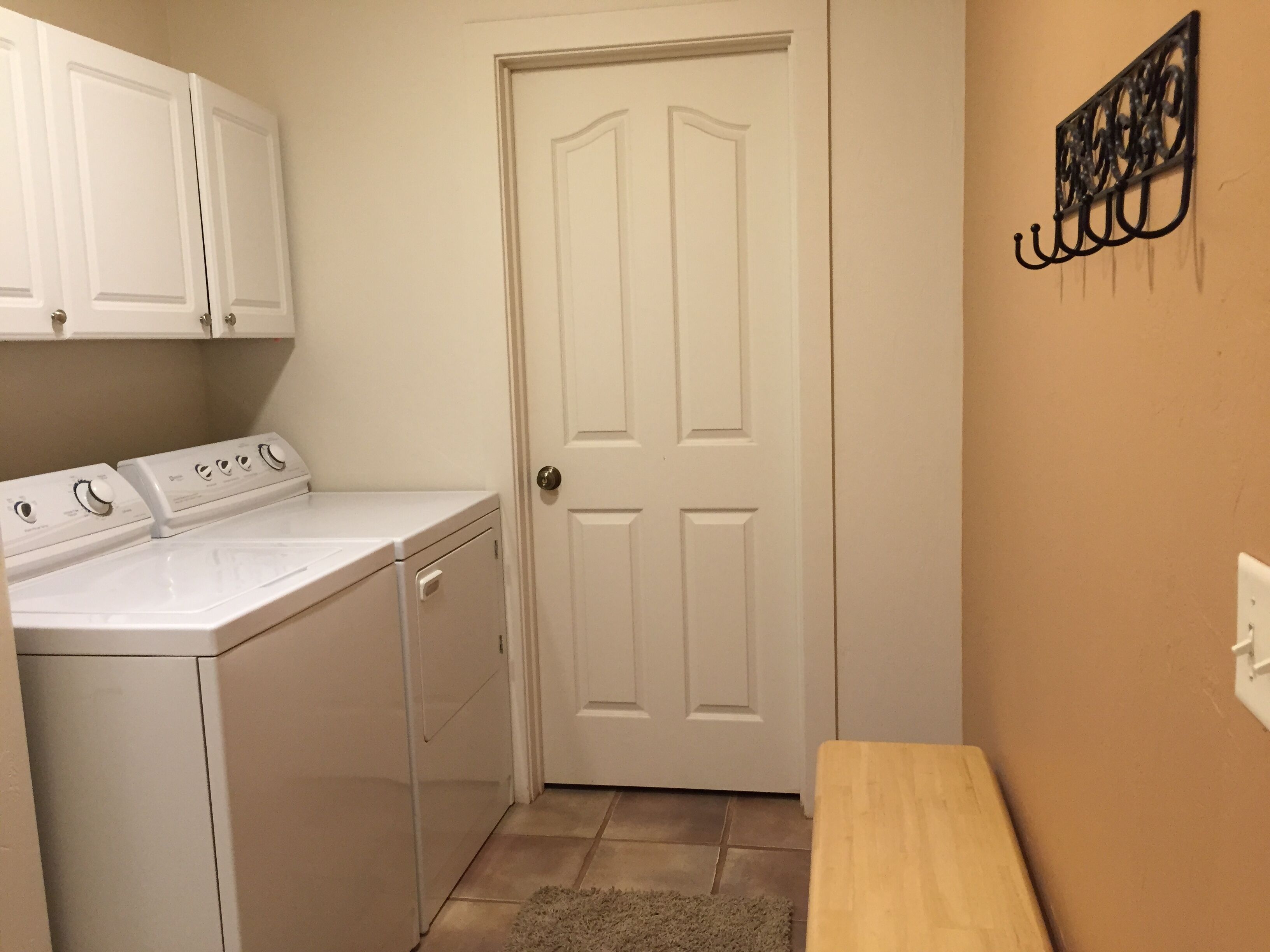 A laundry room with a washer and dryer, a wooden bench, and a door.