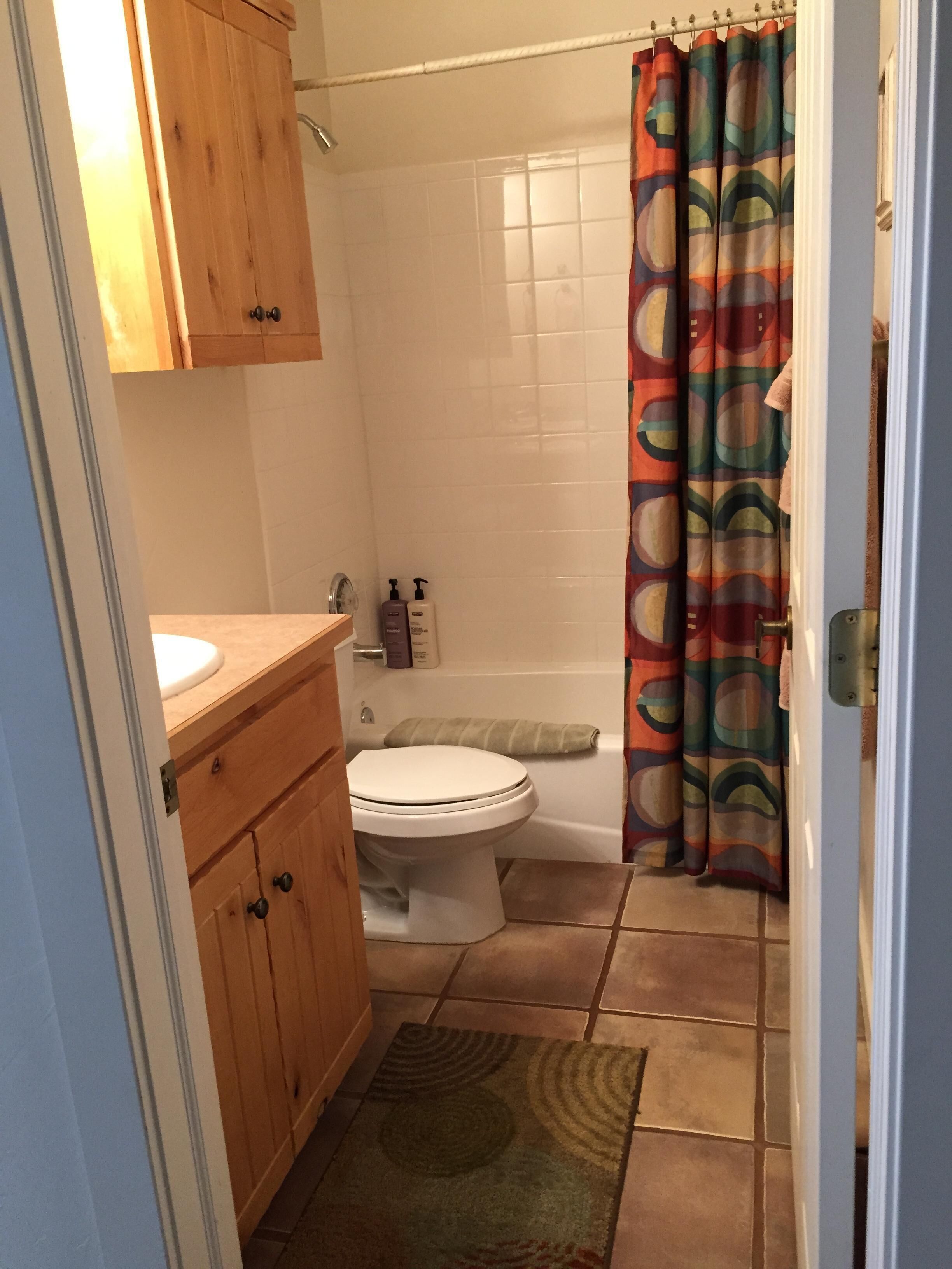 A bathroom with a wooden vanity, a toilet, a shower curtain, and a tiled floor.