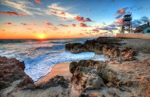 Un paysage côtier avec un phare, une côte rocheuse et un bâtiment entouré d’une clôture blanche.