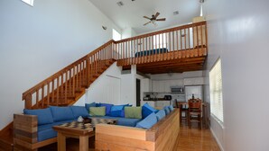 Un salón amplio con una escalera de madera, un conjunto de sofás, una mesa de centro y una cocina al fondo.
