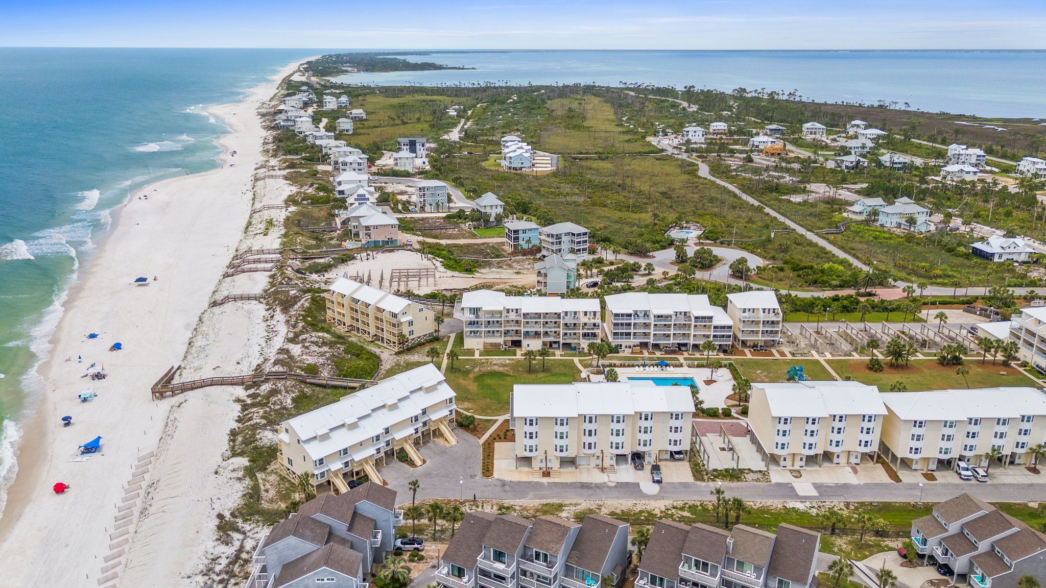 An aerial view of a coastal resort with beachfront properties, a swimming pool, and a boardwalk along the beach.