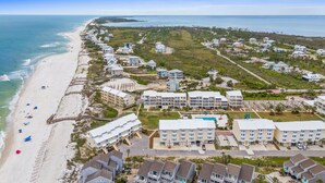 An aerial view of a coastal resort with beachfront properties, a swimming pool, and a boardwalk along the beach.