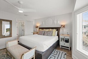 A bedroom with a large bed, bedside tables, a chair, a ceiling fan, and a window with blinds.