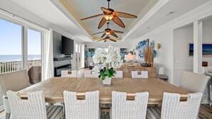 A spacious dining area with a wooden table and wicker chairs, a ceiling fan, and a view of the ocean.